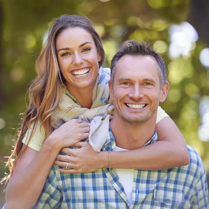 man and woman smiling together outdoors near trees