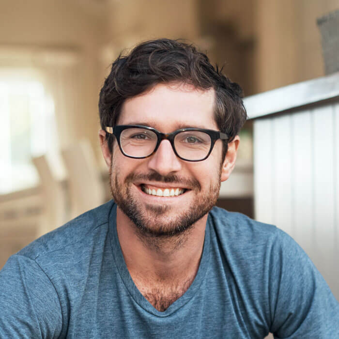 adult man wearing black-rimmed glasses sitting on his porch and smiling